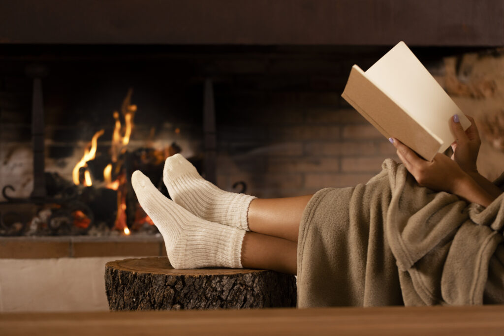 Girl reading in a cozy environment with fireplace.